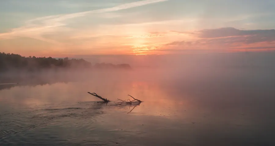 Photographer standing at a misty lake at first light