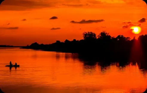 Fisherman silhouetted on a lake under a deep orange sunset