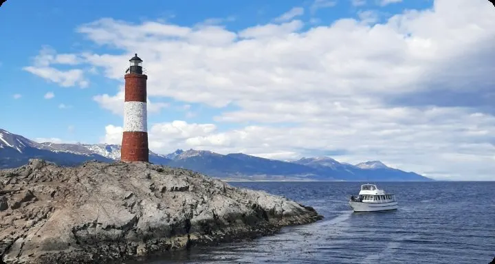 Red and white lighthouse on a rocky point with mountains and boat