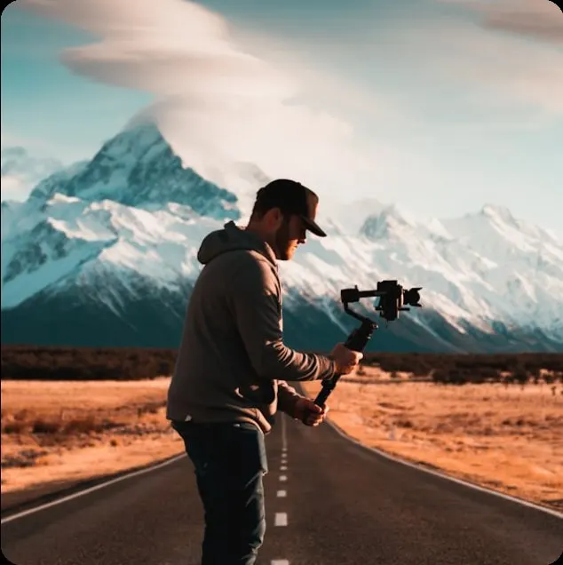 Traveler with camera gimbal on an empty road toward snowy peaks